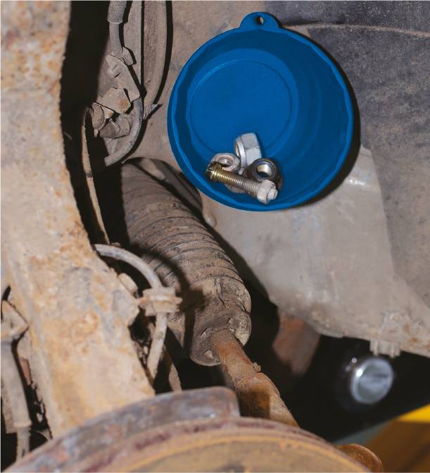 Ein blauer Kunststoffdeckel ist am Fahrzeugunterboden mit Schrauben und einer Mutter darin befestigt. Sichtbare Teile sind rostig.