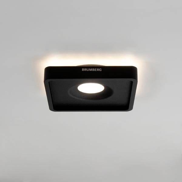 Ein quadratischer, schwarzer Deckenstrahler mit integriertem LED-Licht, montiert an einer weißen Decke und leuchtet nach unten.