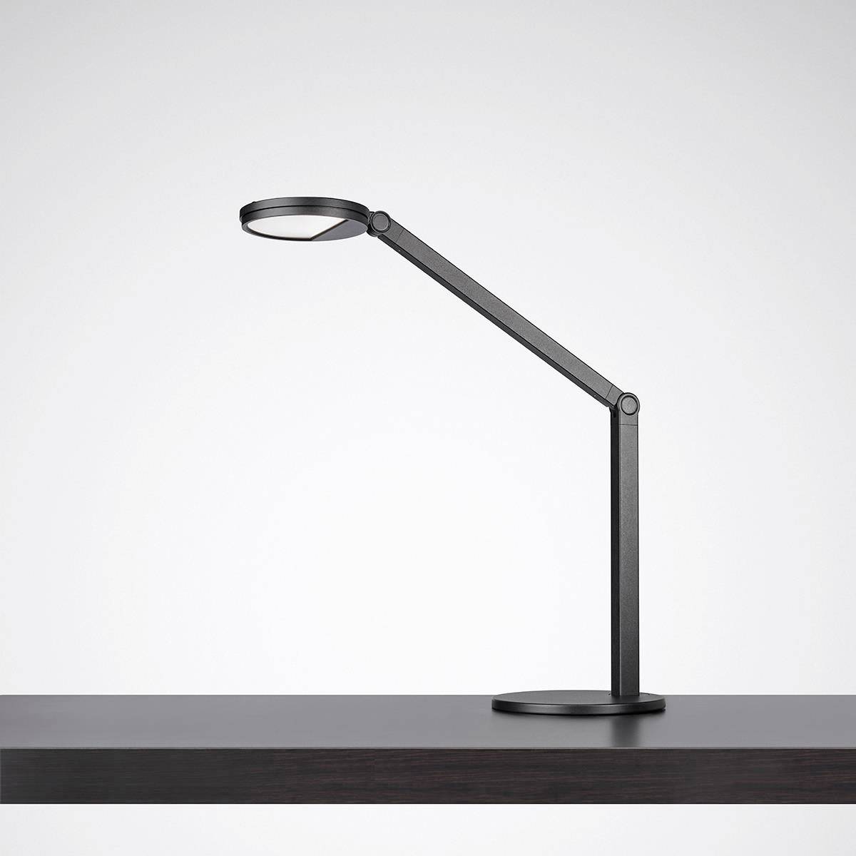 Schwarze Schreibtischlampe mit verstellbarem Arm auf einem Tisch, beleuchtet eine kleine Fläche.