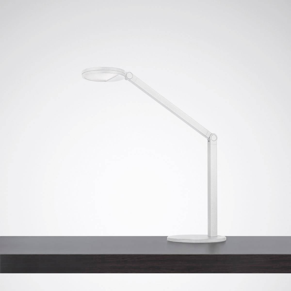 Eine minimalistische, moderne Tischlampe mit flexiblem Hals steht auf einem dunklen Holztisch vor einem neutralen Hintergrund.