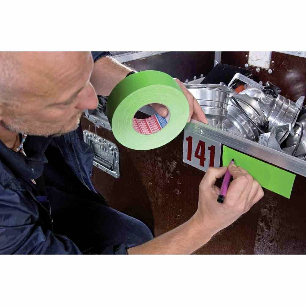 Ein Mann beschriftet mit einem Stift grünes Klebeband, das an einer Kiste angebracht ist. Die Kiste enthält Beleuchtungsequipment.