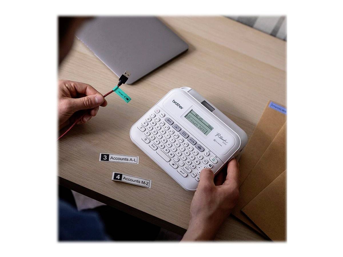 Person arbeitet mit einem Etikettendrucker und etikettiert USB-Kabel. Auf dem Tisch liegen ein Laptop und Umschläge.