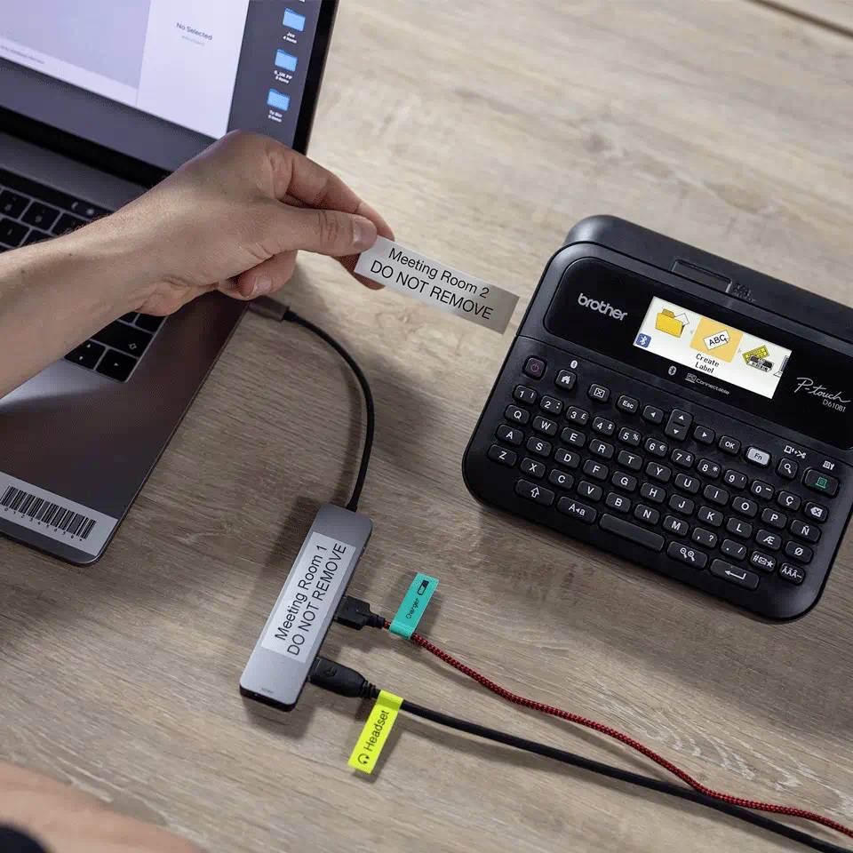 Eine Hand hält ein beschriftetes Etikett mit der Aufschrift 'Meeting Room 2 - DO NOT REMOVE'. Im Hintergrund ein Etikettendrucker.