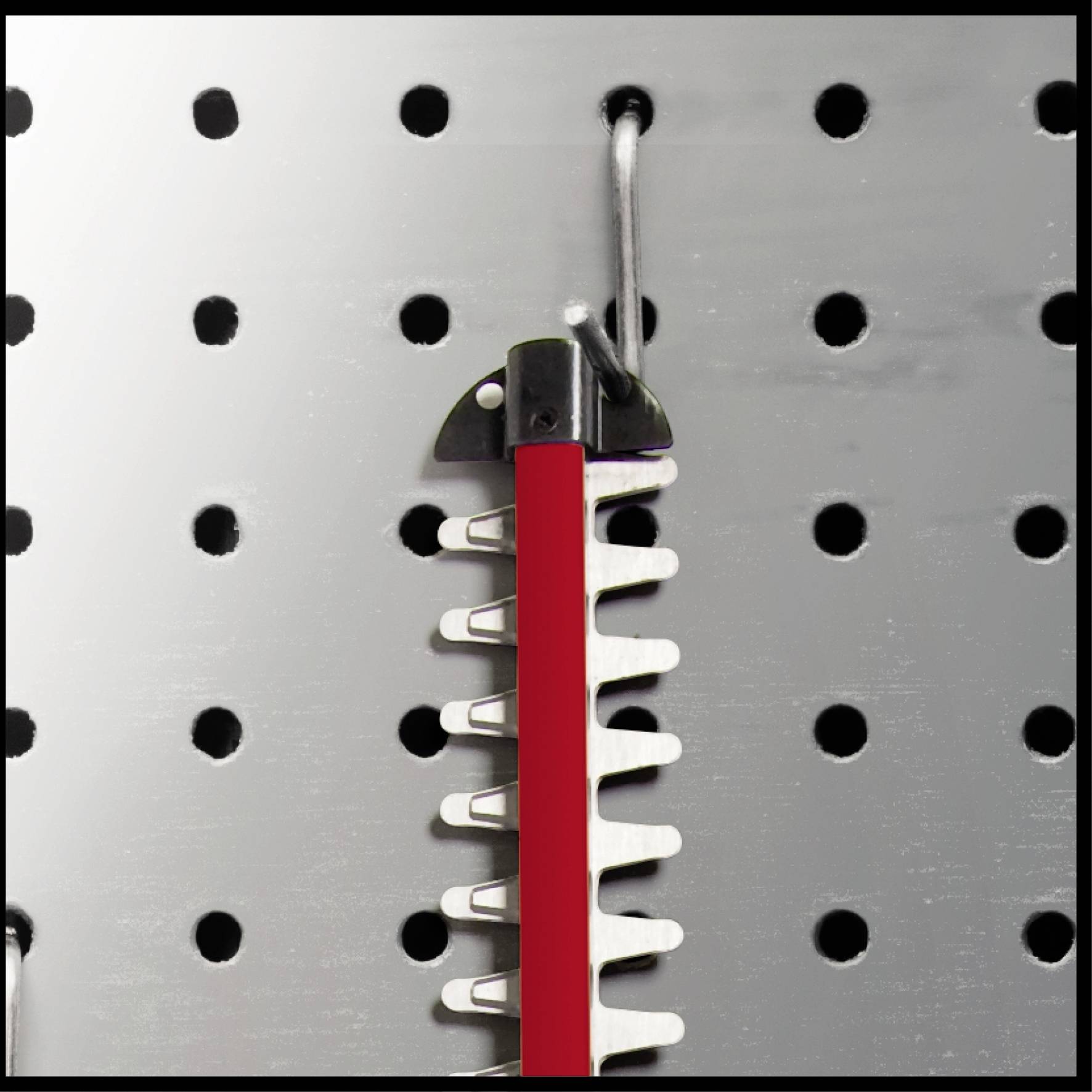 Ein rotes Werkzeug hängt an einem Haken auf einer Lochwand. Es hat gezackte Metallkanten, die für Schneidearbeiten geeignet sind.