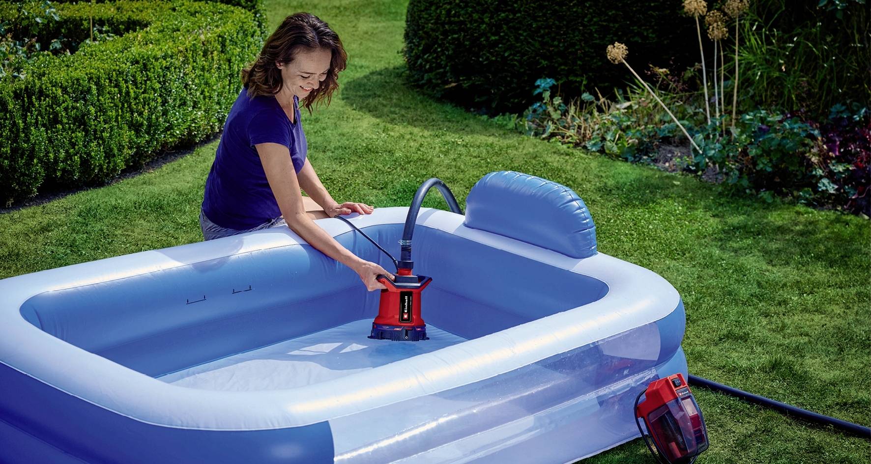 Eine Frau pumpt in einem Garten ein aufblasbares Schwimmbecken mit einer elektrischen Luftpumpe auf.