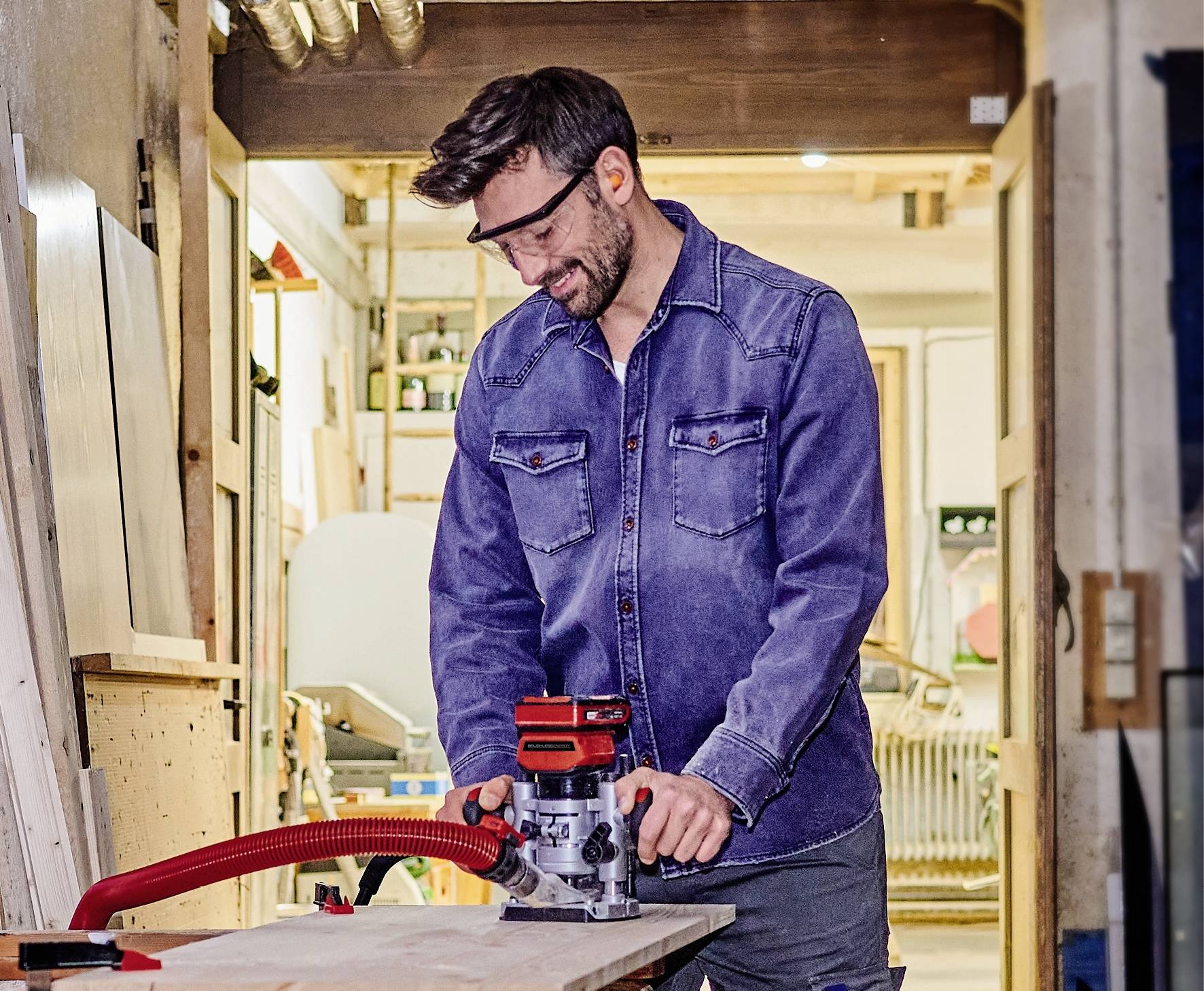 Ein Mann trägt Schutzbrille und bedient eine Tischfräse in einer Werkstatt. Er konzentriert sich auf die Holzbearbeitung.