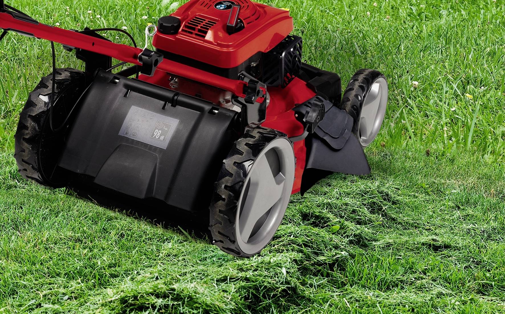 Ein roter Rasenmäher mäht grünes Gras. Hinten sind frisch geschnittene Grasstreifen deutlich zu erkennen.