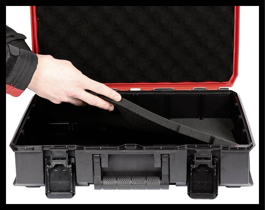 Eine Hand legt eine Schaumstoffeinlage in einen offenen, leeren schwarzen Werkzeugkoffer mit rotem Rand.