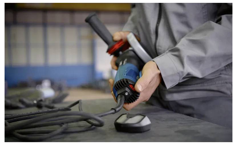 Person mit einem Elektrowerkzeug mit Kabel, bereitet sich auf die Verwendung an einer Werkbank in einer Werkstattumgebung vor.