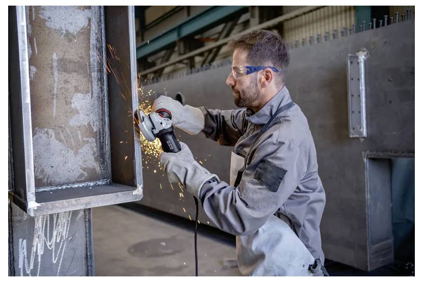 Ein Arbeiter in Schutzausrüstung verwendet eine Winkelschleifer zum Schneiden von Metall, wobei Funken sprühen, in einer industriellen Umgebung.