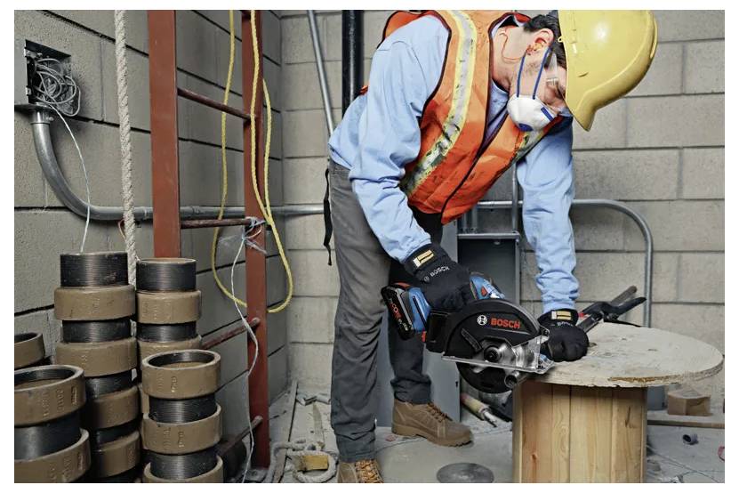 Ein Bauarbeiter in Schutzausrüstung schneidet Metall auf einer Holzspule mit einem Bosch-Elektrowerkzeug in einer Industrieumgebung.