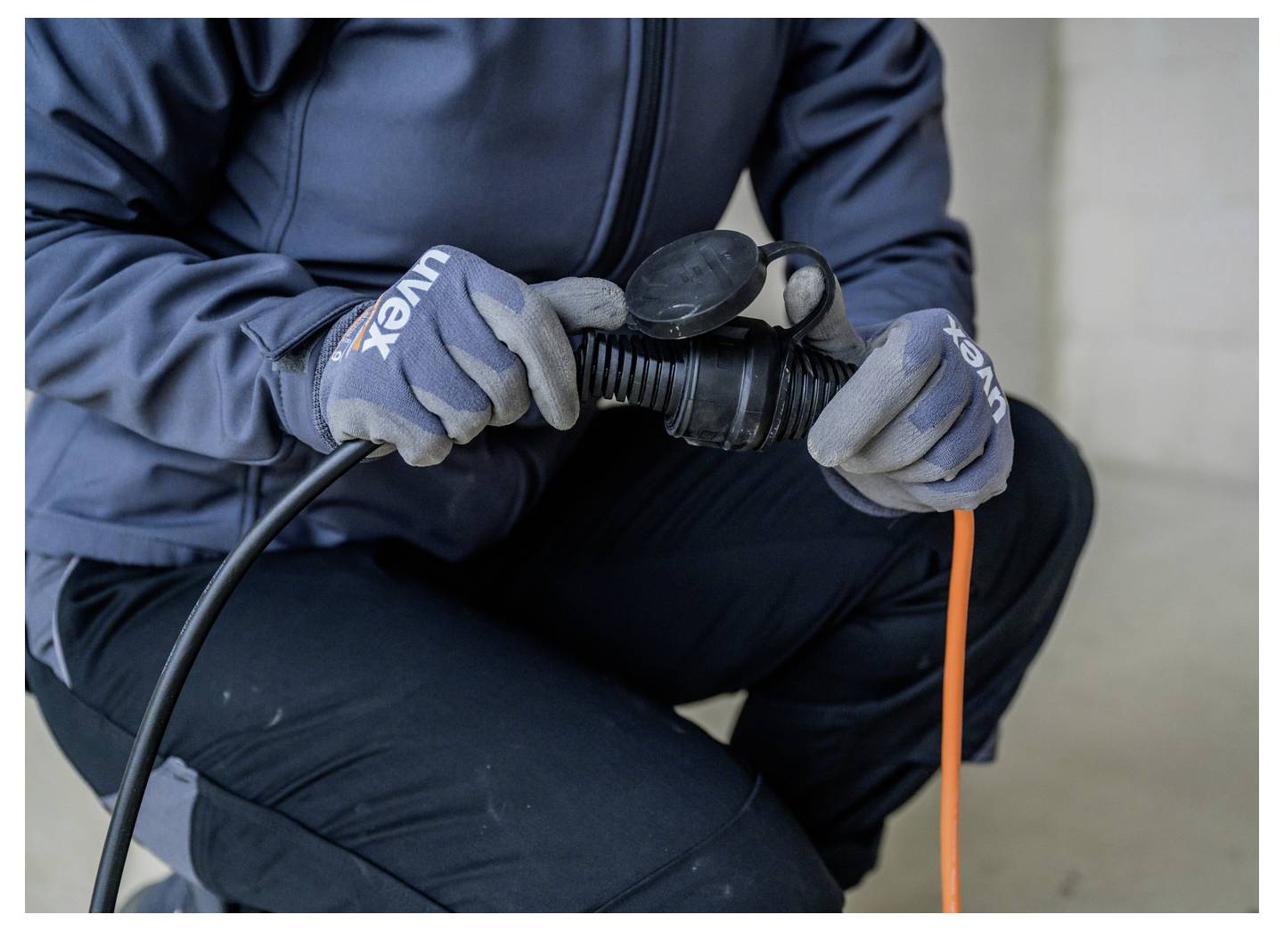 Arbeiter in Handschuhen verbindet ein Kabel mit einer schwarzen Außenstrom-Steckdose oder einem Stecker, während er in die Hocke geht.
