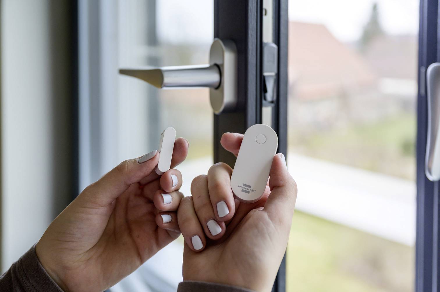 Eine Person installiert einen Tür- oder Fenstersensor an einem geöffneten Fenster. Der Sensor dient zur Überwachung der Öffnungsbewegung.