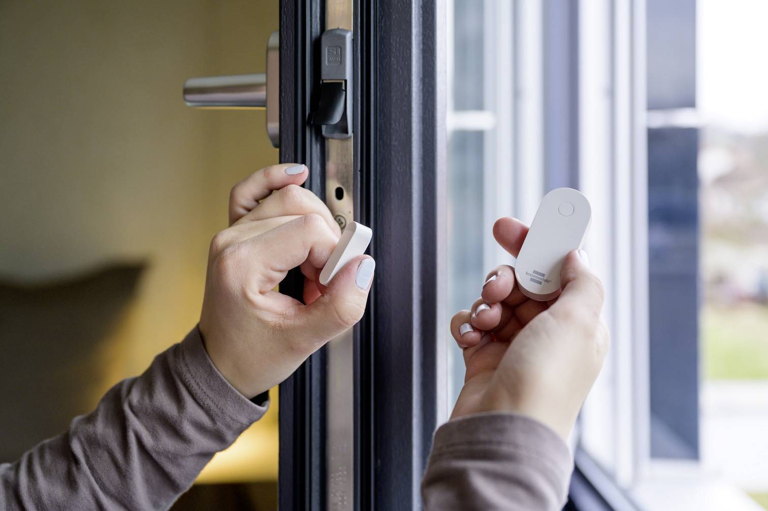Eine Person hält zwei weiße Sensoren an einem offenen Fensterrahmen in der Hand.