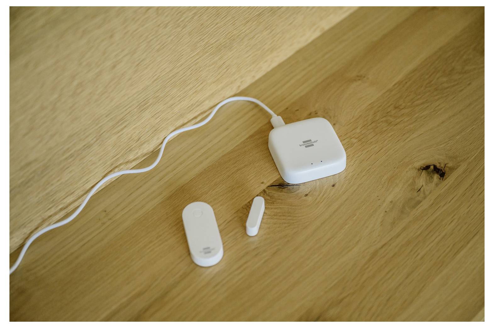 Weißes kabelloses Ladeetui mit Kabel auf einem Holztisch, mit zwei kleinen weißen Ohrhörer-Teilen daneben.