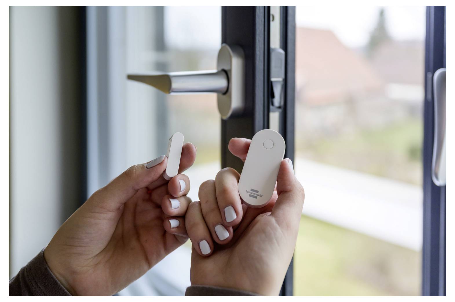 Hände halten einen kabellosen Tür-/Fenstersensor in der Nähe eines offenen Fensterverriegelungsmechanismus, was auf die Installation eines Heimsicherheitssystems hindeutet.