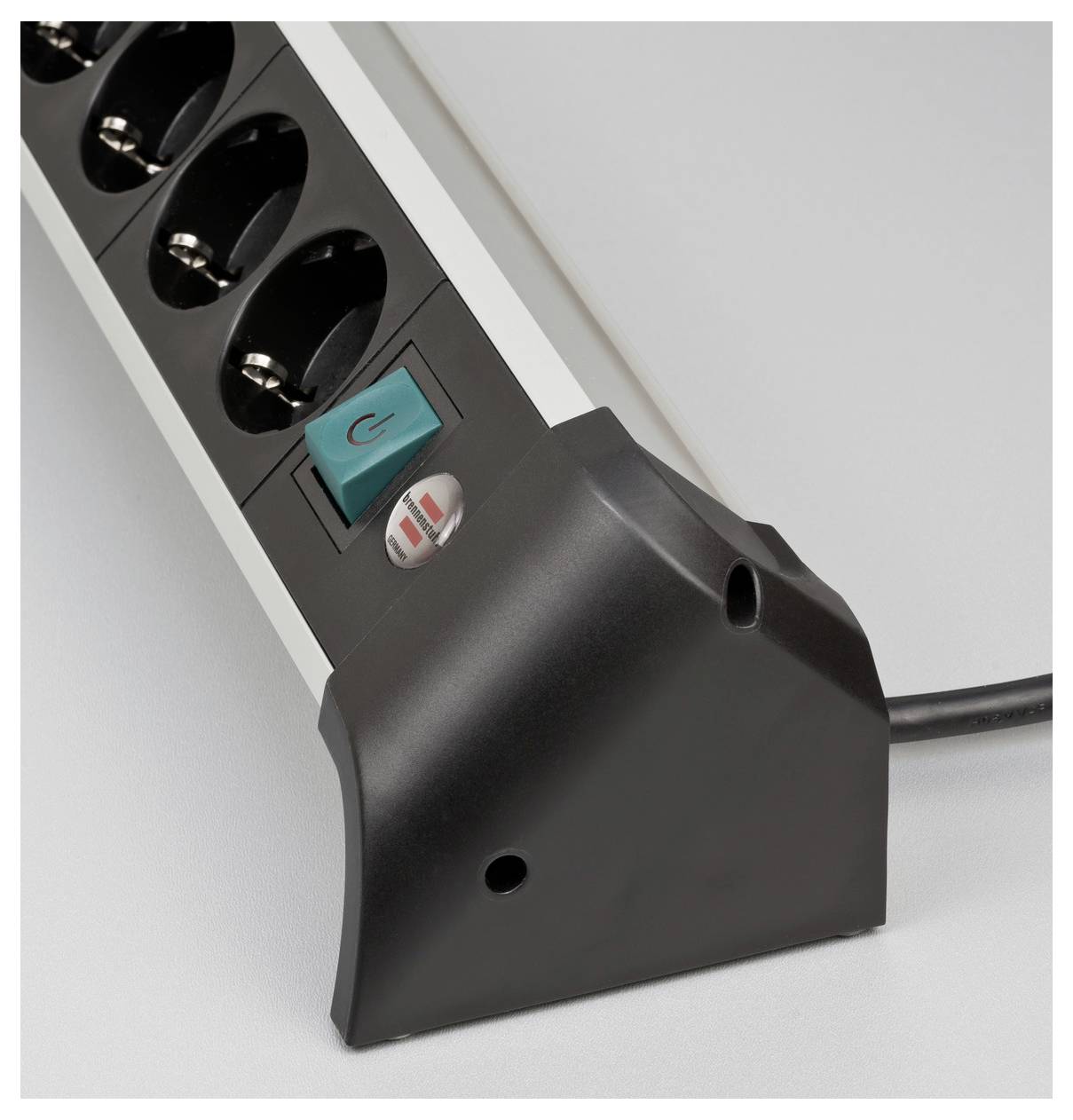 Nahaufnahme einer Steckerleiste mit mehreren Steckdosen, einem türkisfarbenen Ein-/Ausschalter und einem angeschlossenen schwarzen Stecker oder Adapter an einem Ende.