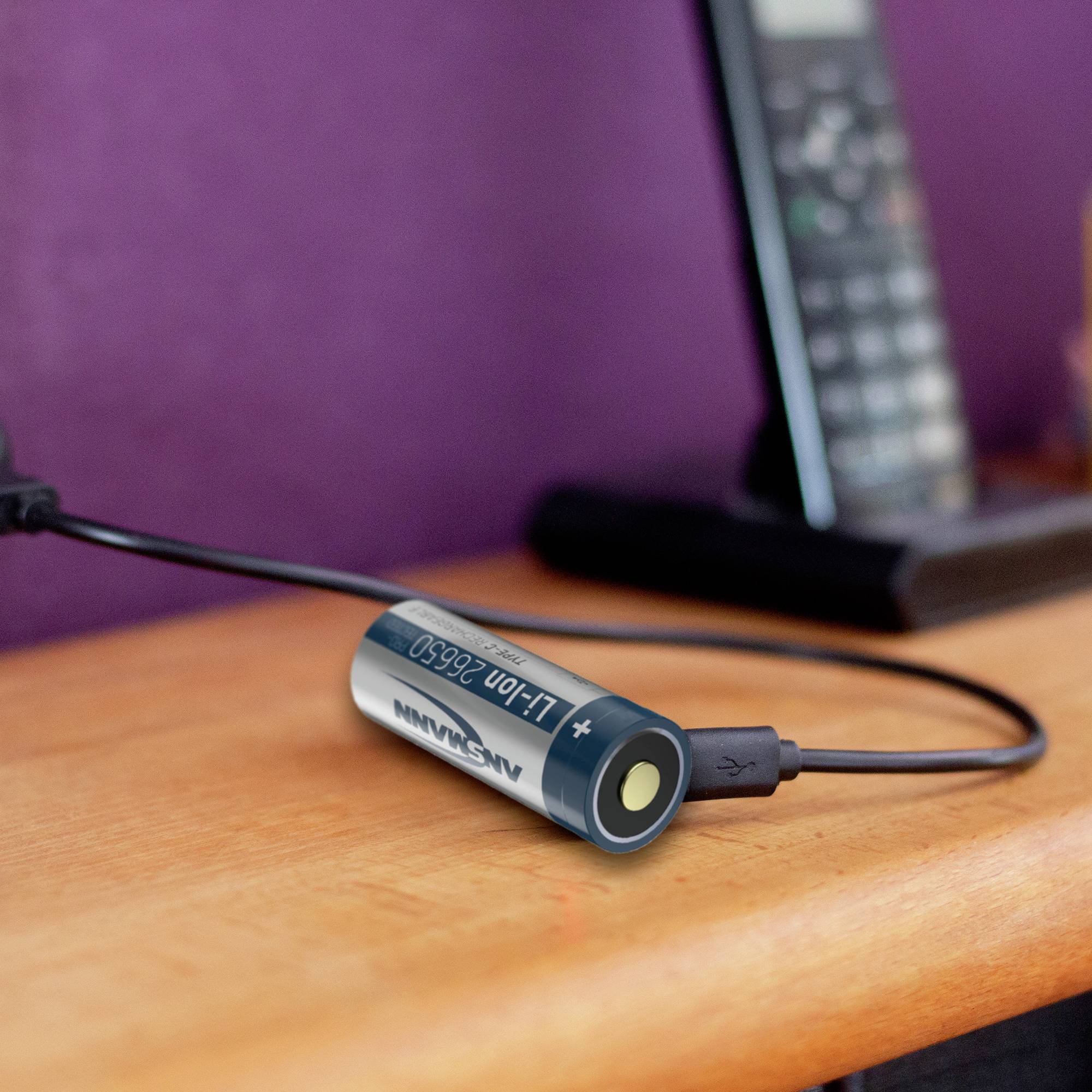 Ein Telefon wird auf einem Tisch aufgeladen mit einem AA-Akku-Adapter, der über ein USB-Kabel verbunden ist.