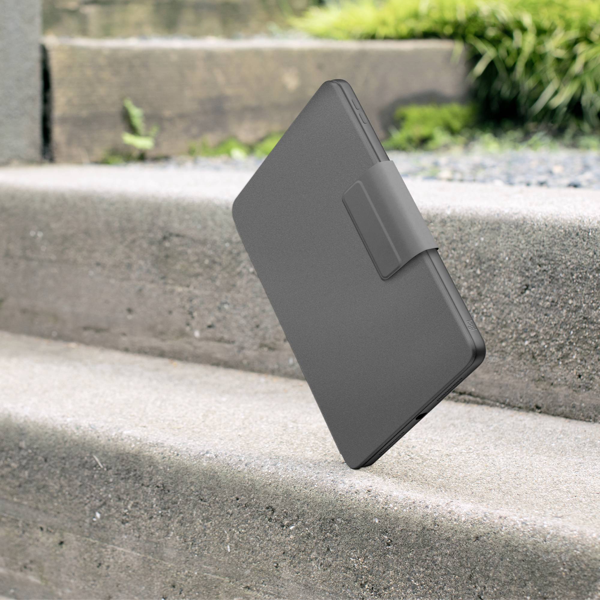 Ein schwarzer, geschlossener E-Book-Reader in einem Schutzetui liegt schräg auf einer Steintreppe, im Hintergrund sind grüne Pflanzen.