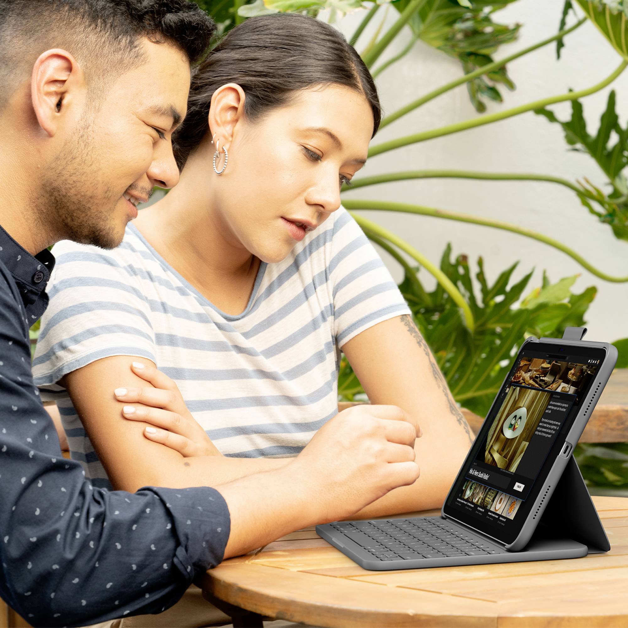 Ein Mann und eine Frau betrachten zusammen ein digitales Tablet mit einem Tastaturständer. Sie scheinen in ein Gespräch vertieft zu sein.