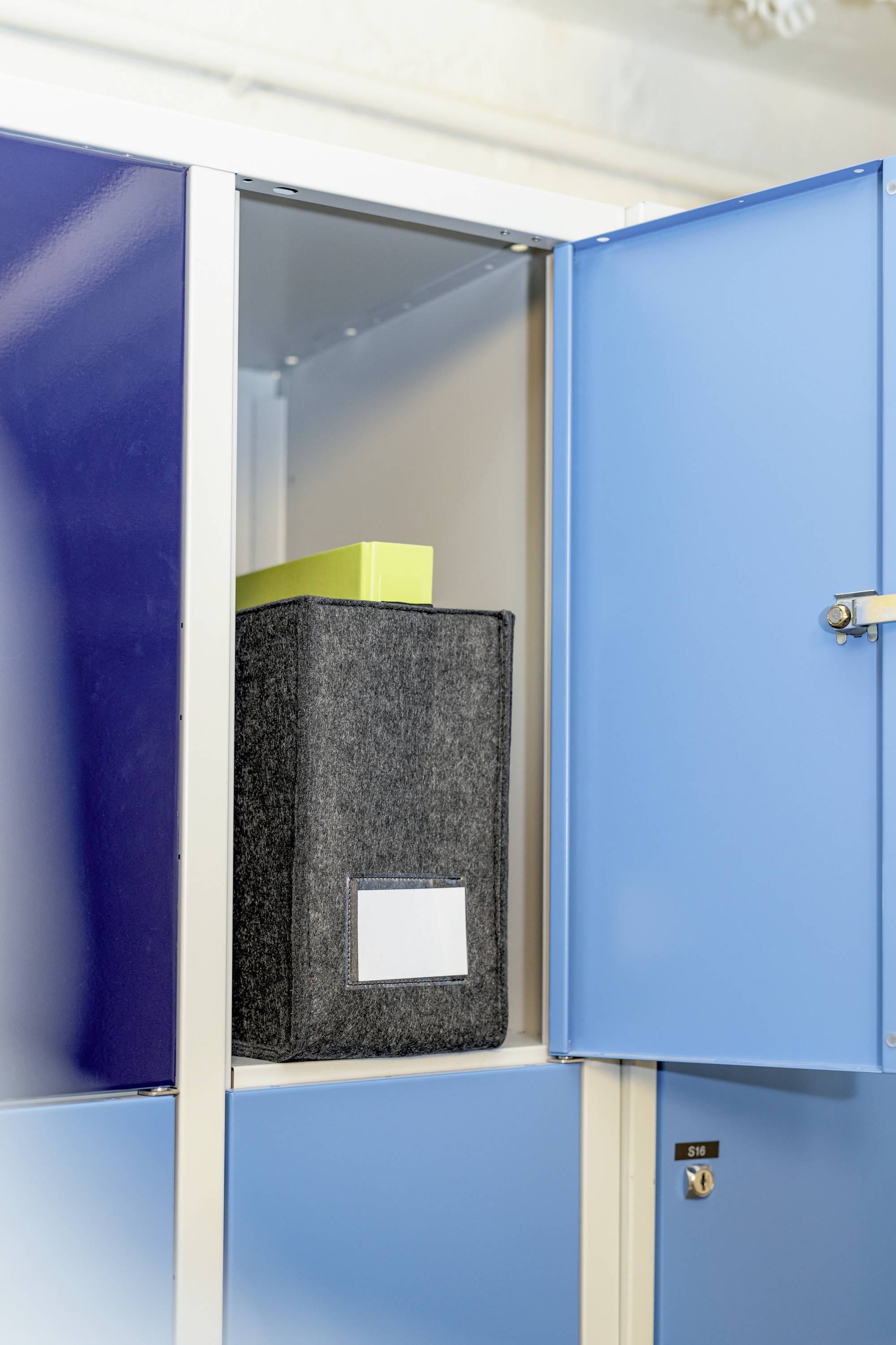 Ein geöffneter blauer Schrank zeigt einen schwarzen Ablageordner und eine gelbe Box, die darin aufbewahrt werden.