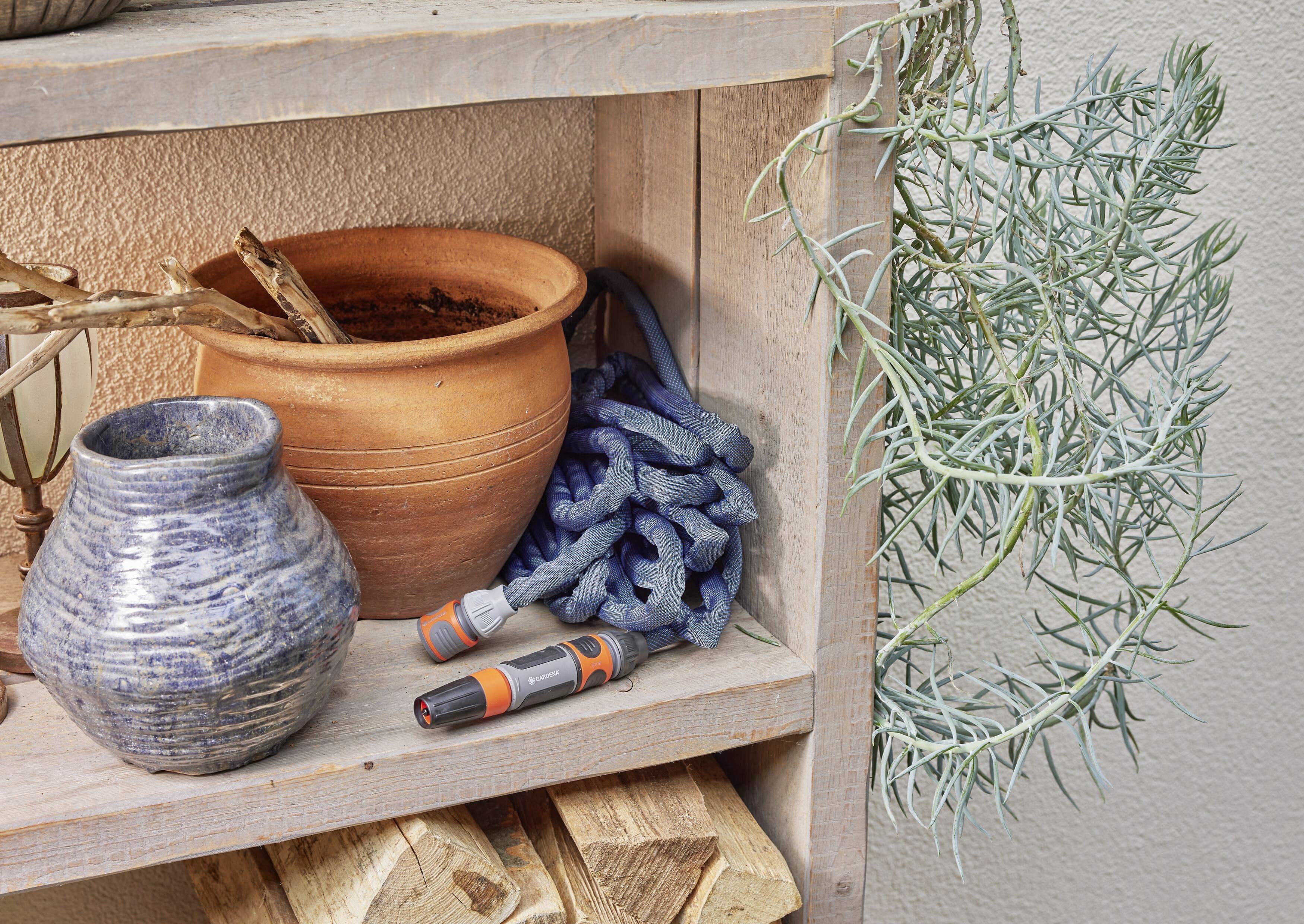 Ein Holzregal mit Blumentopf, Gießschlauch, sprießender Pflanze und Vase. Holzteile und Wand bilden den Hintergrund.