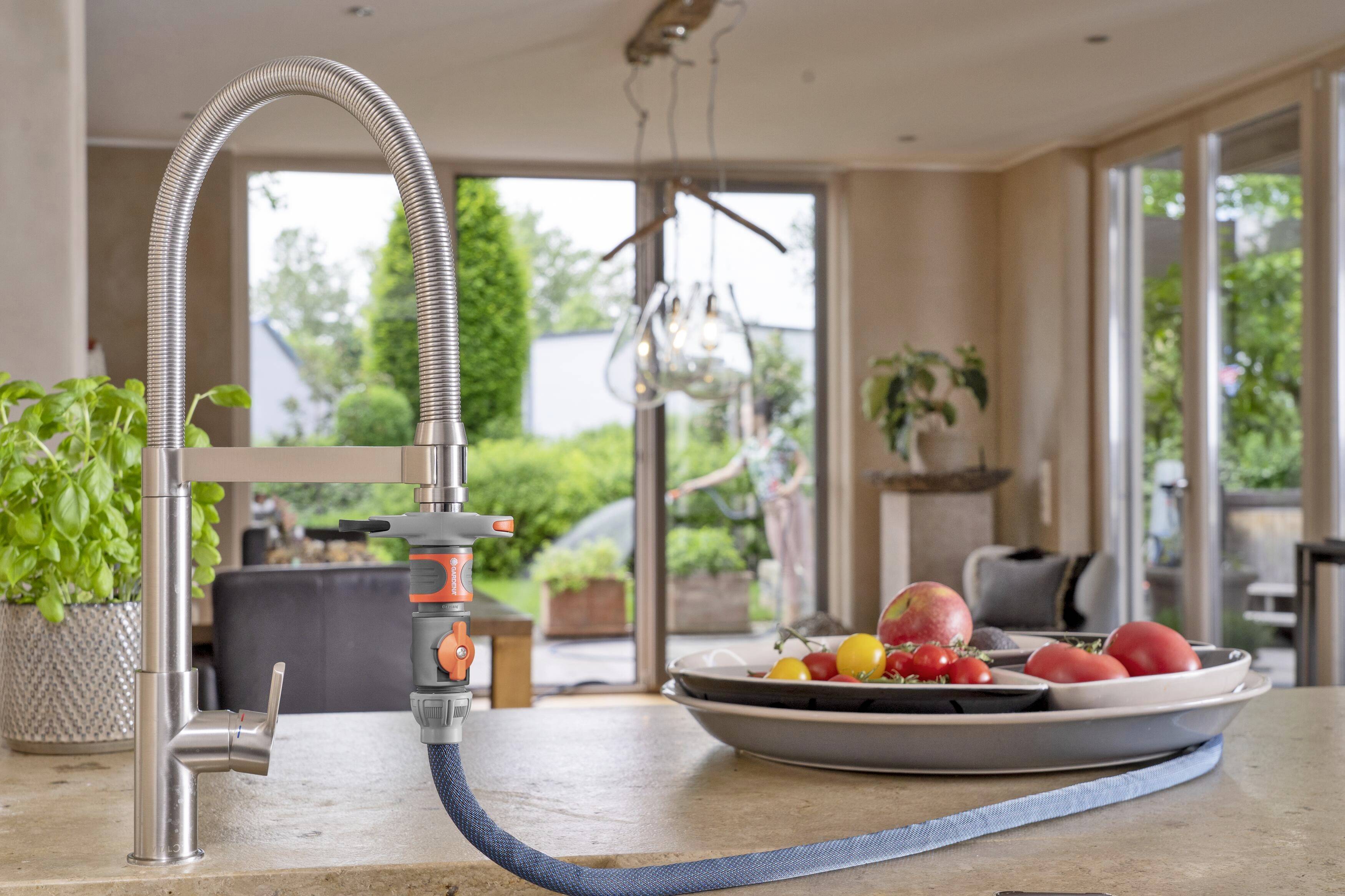 Ein Wasserhahn in einer modernen Küche mit Blick auf einen Garten. Auf der Arbeitsfläche befinden sich Obstschalen mit Äpfeln und Tomaten.