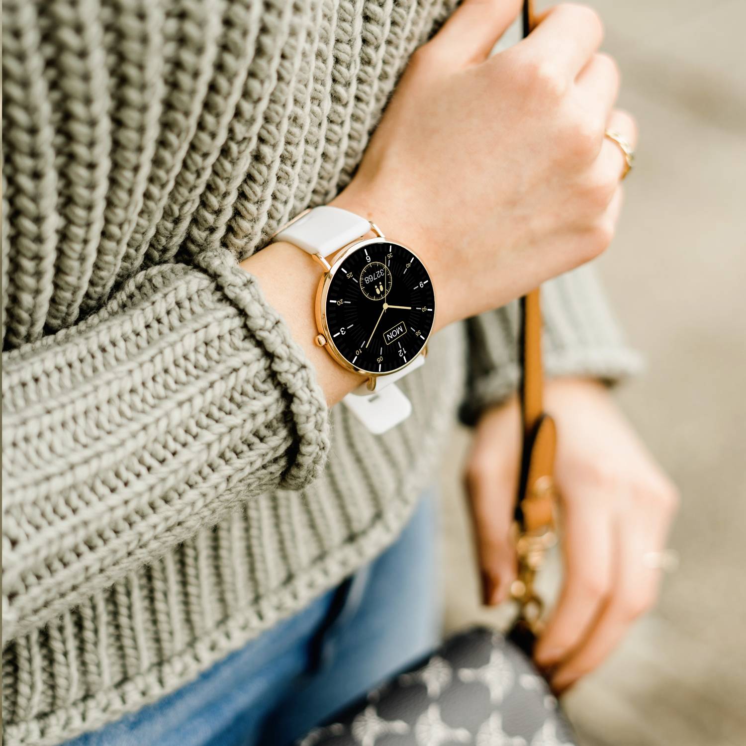 Eine Person trägt eine elegante Armbanduhr mit schwarzem Zifferblatt und goldenen Details. Sie hält eine braune Tasche.