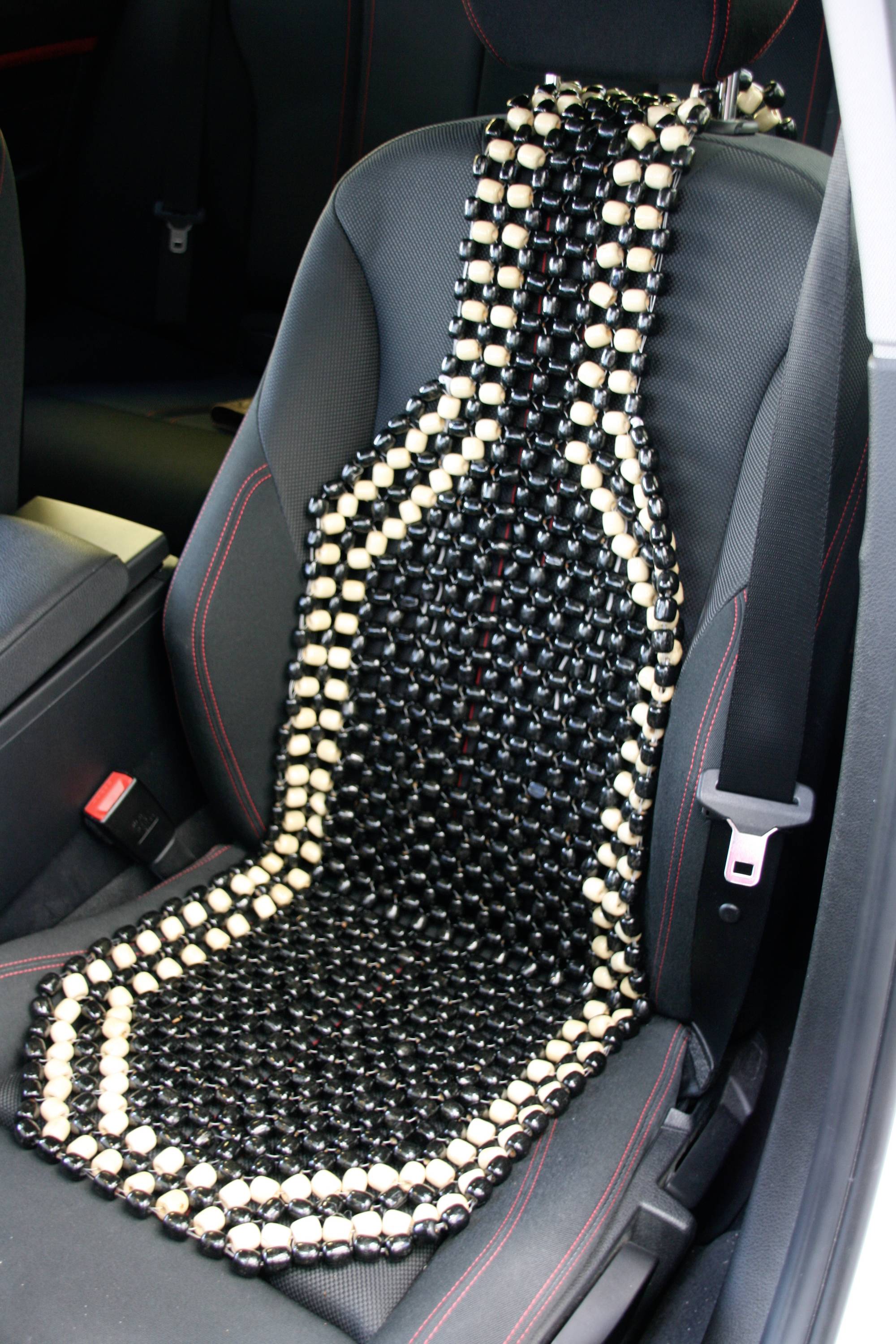 Sitzauflage mit schwarzen und hellen Holzkugeln auf einem Autositz für Massage und Belüftung.