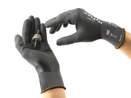 Zwei Hände in schwarzen Handschuhen halten ein kleines Zahnrad. Die Handschuhe sind für präzise Arbeiten geeignet.