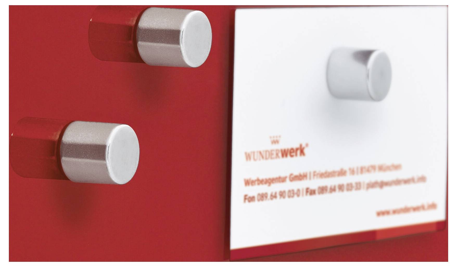 Nahaufnahme eines rot-weißen Anzeigefelds mit zwei silbernen zylindrischen Knöpfen und dem Logo „WUNDERWERK" sowie Kontakttext auf der rechten Seite.