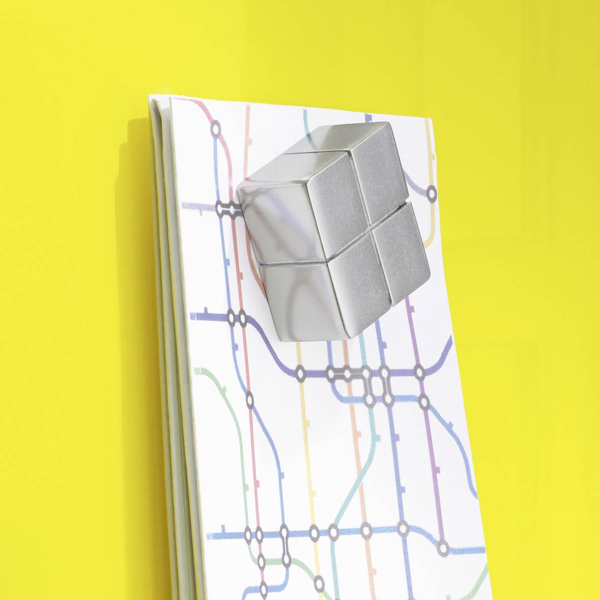 Ein silbernes magnetisches Puzzle in Würfelform haftet an einem farbenfrohen Stadtplan auf gelbem Hintergrund.