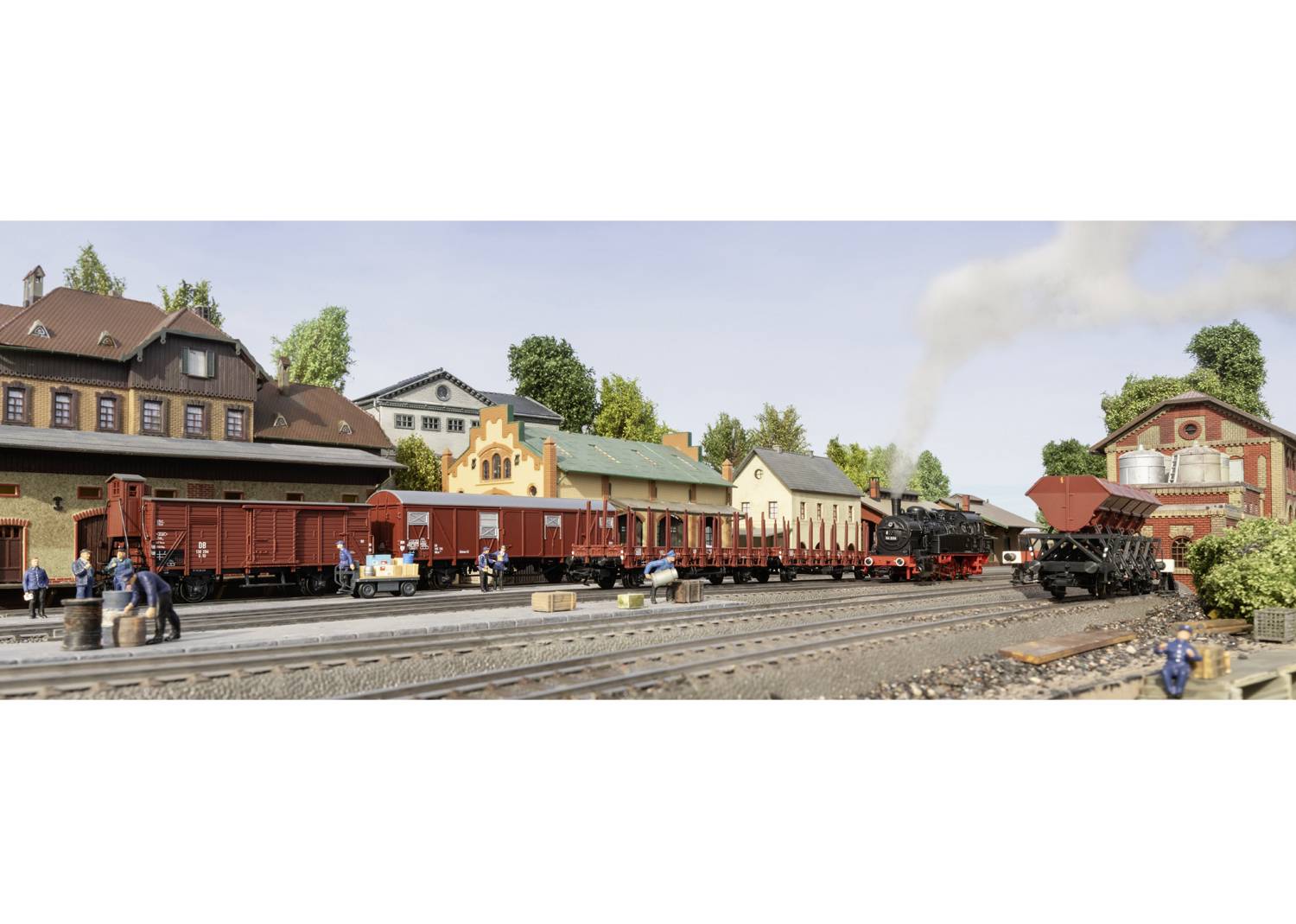 Eisenbahnmodelllandschaft mit Güterzug und Dampflokomotive in einer Stadtkulisse; Menschen beleben die Szene am Bahnhof.