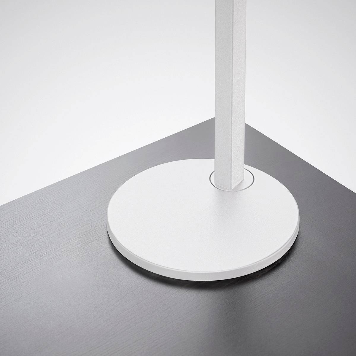 Eine weiße vertikale Stange steht auf einem runden weißen Sockel, der auf einer dunklen Oberfläche ruht.