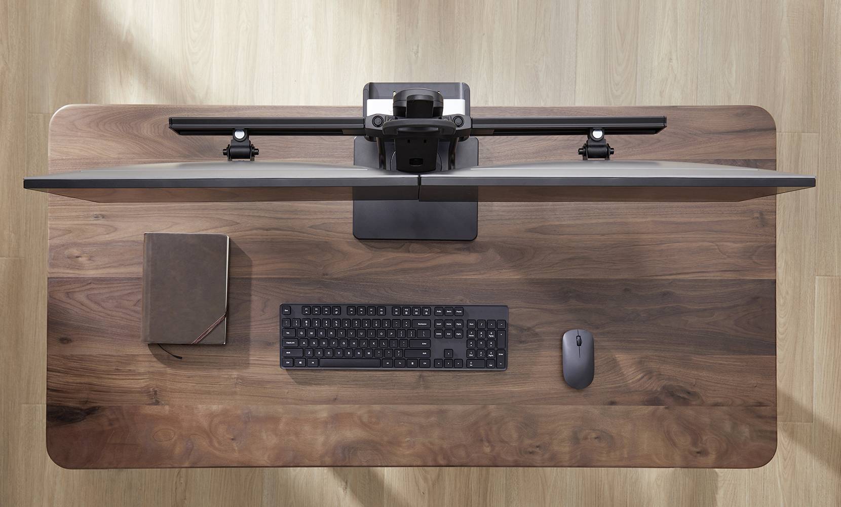 Ein Schreibtisch aus Holz mit einem geschlossenen Laptop, einer Tastatur und einer Maus von oben gesehen.