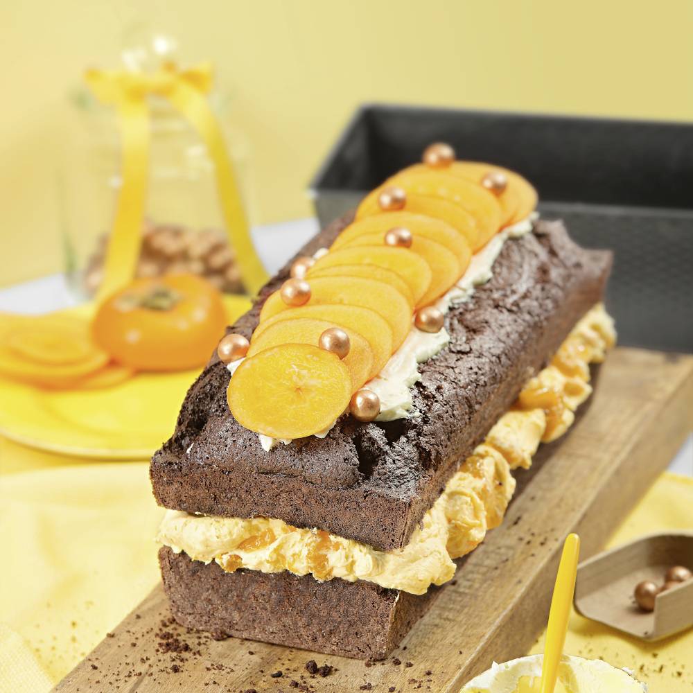 Ein Schokoladenkuchen mit Schlagsahne, dekoriert mit orangenen Fruchtscheiben und goldenen Kugeln, auf einem Holzbrett serviert.