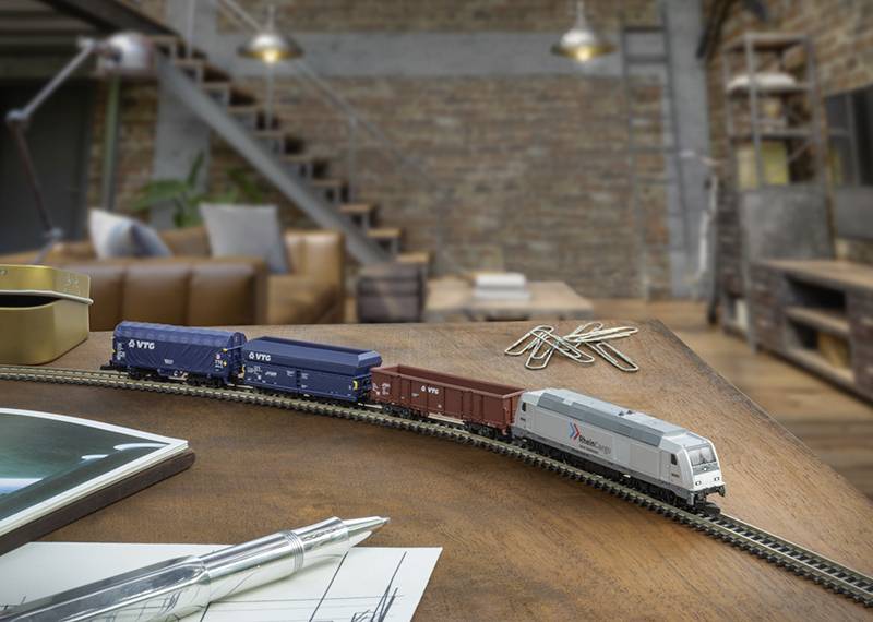 Ein kleiner Modelzug mit mehreren Waggons ist auf einem Holztisch in einem Wohnzimmer im Industriestil mit einer Treppe und einem Ledersofa aufgebaut.