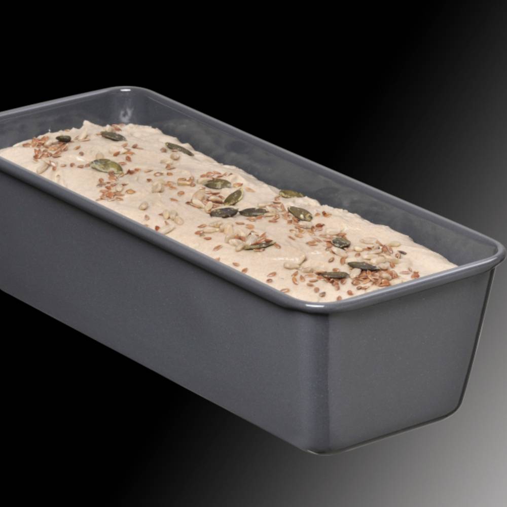 Eine rechteckige Backform mit ungebackenem Teig, bestreut mit Kürbis- und Leinsamen, auf schwarzem Hintergrund.