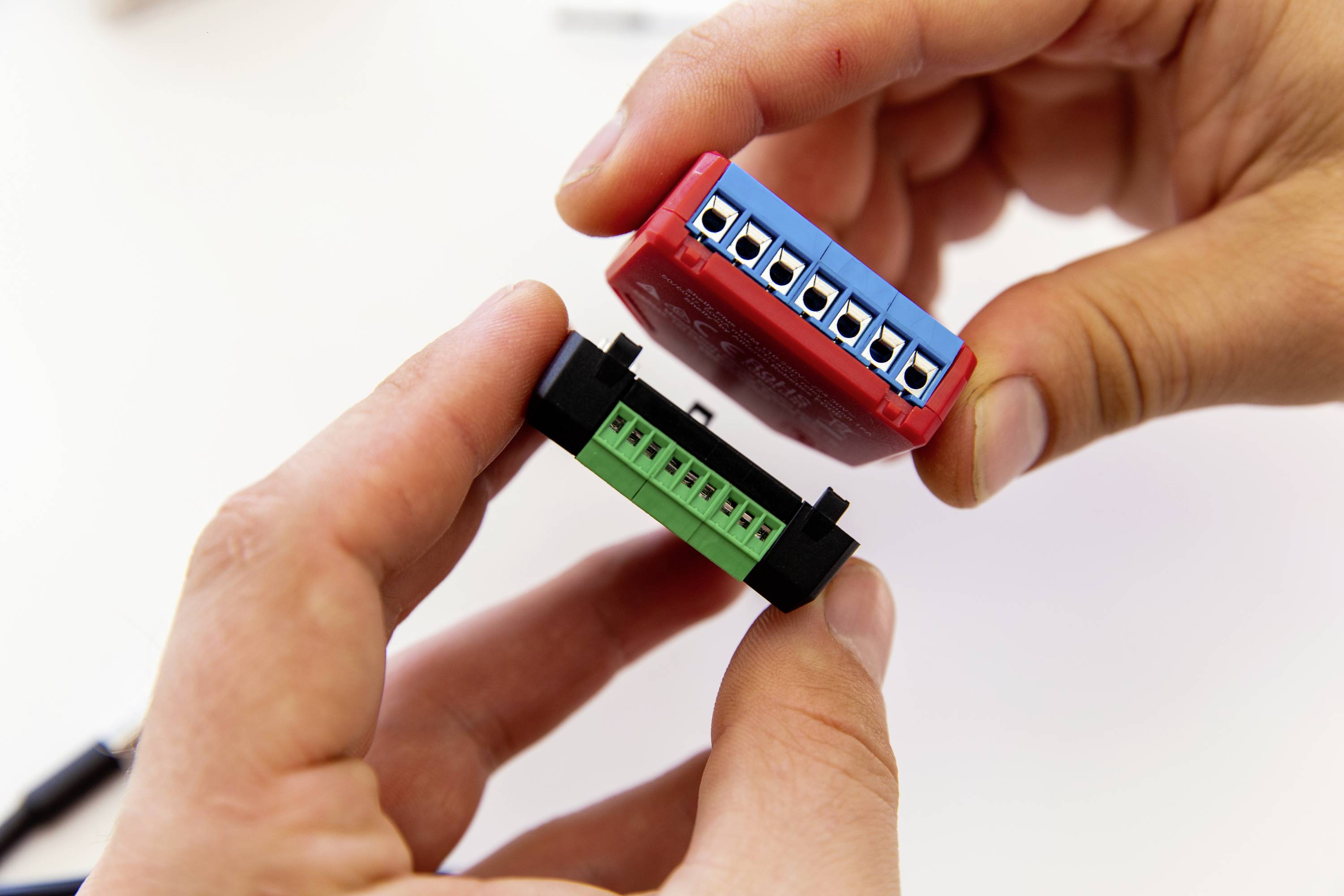 Zwei Hände halten elektronische Bauteile mit farbigen Anschlüssen, die zusammengefügt werden.