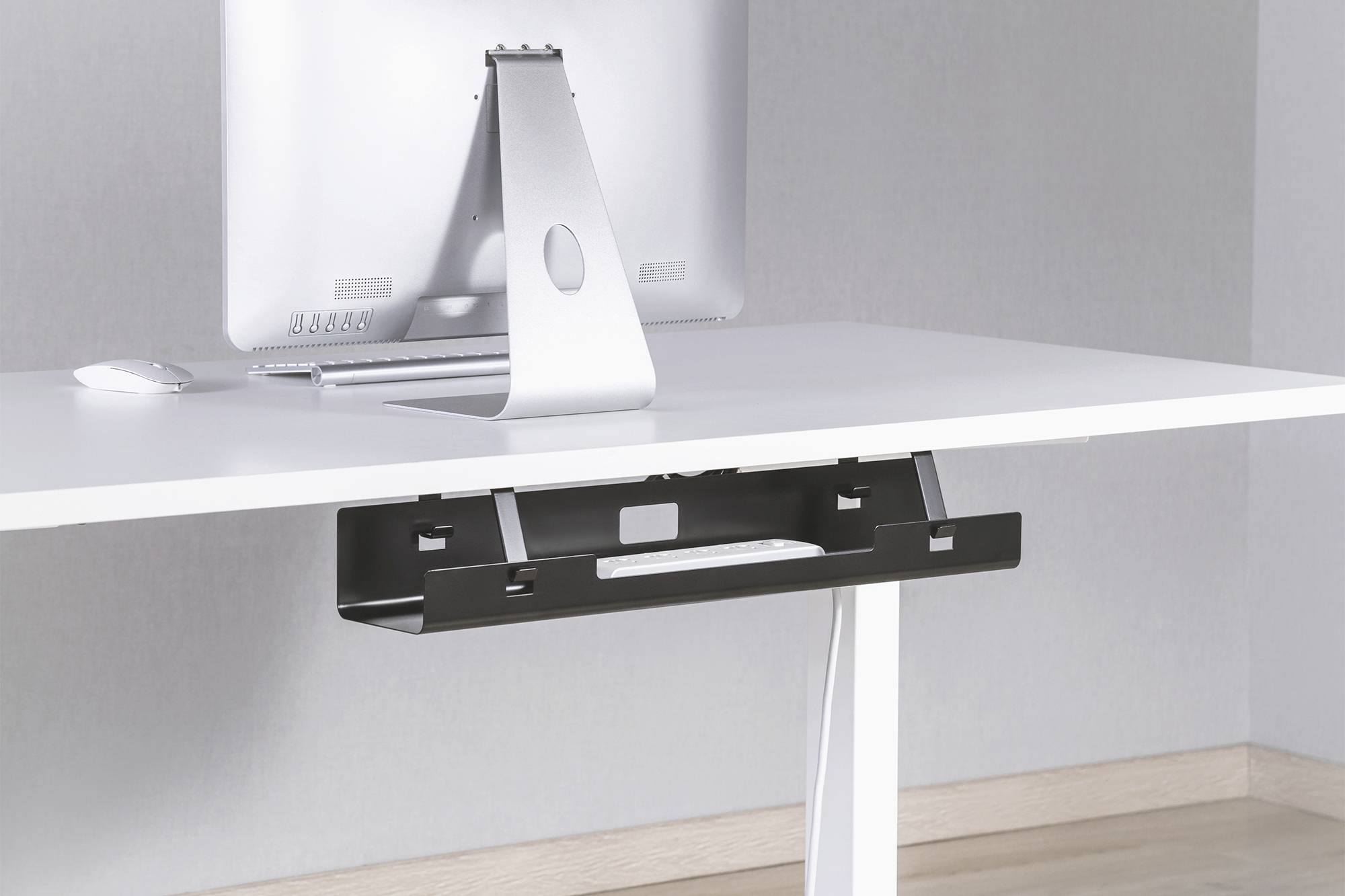 Ein Computerbildschirm auf einem weißen Schreibtisch. Darunter ist ein schwarzer Kabelkanal montiert, der Kabel ordentlich versteckt.