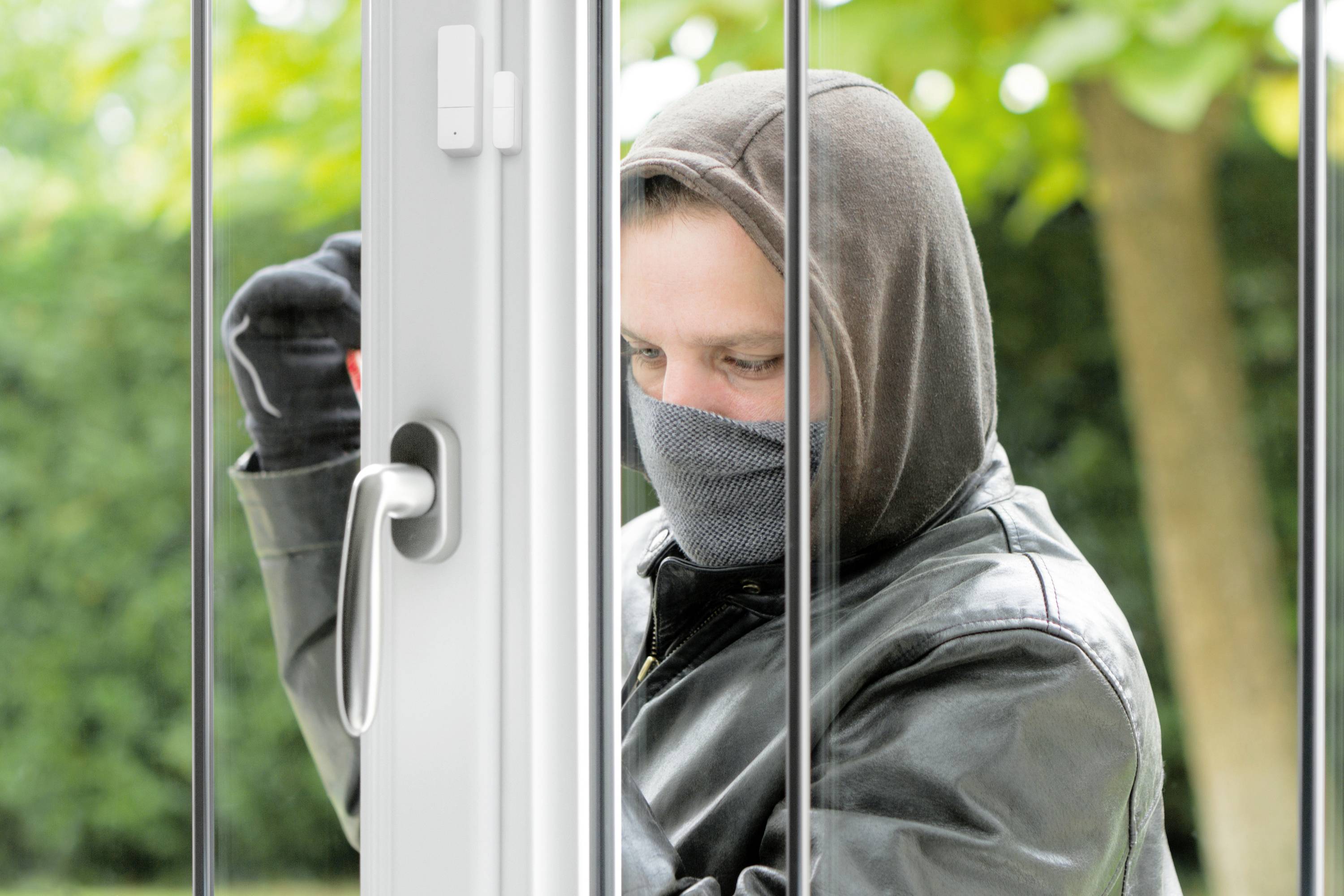 Eine vermummte Person versucht, mit einem Werkzeug ein Fenster von außen zu öffnen.