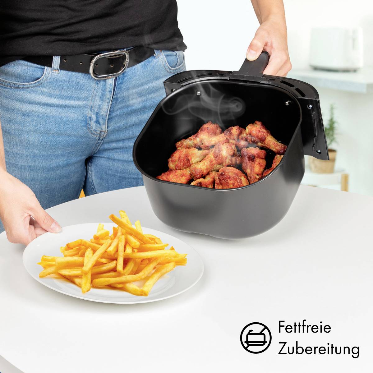 Eine Person legt dampfende, frittierte Hähnchenflügel aus einer Fritteuse auf einen Teller mit Pommes frites, symbolisiert fettfreies Kochen.