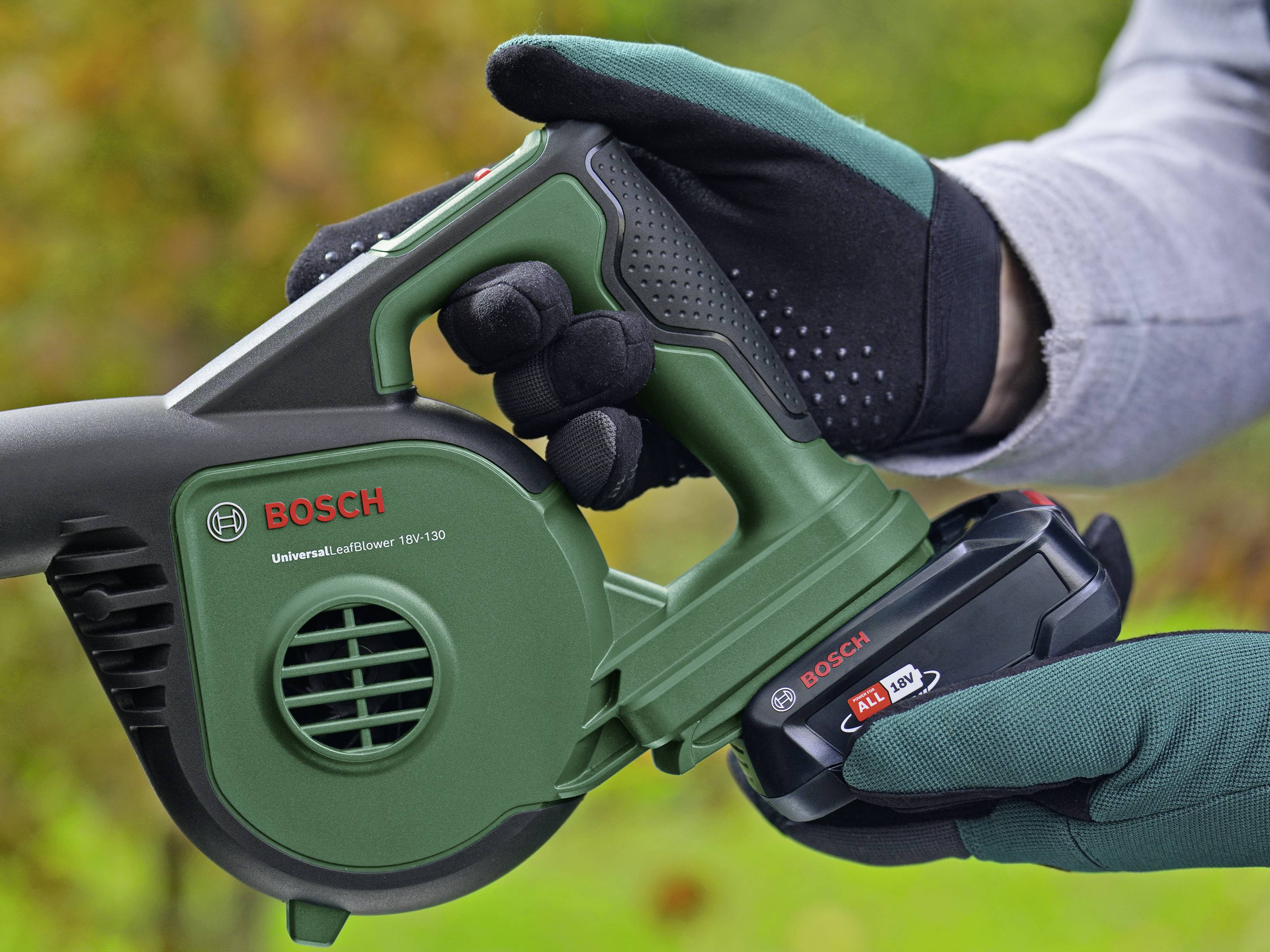 Eine Person hält einen grünen Bosch-Laubbläser in der Hand. Eine Batterie wird gerade in das Gerät eingesetzt.