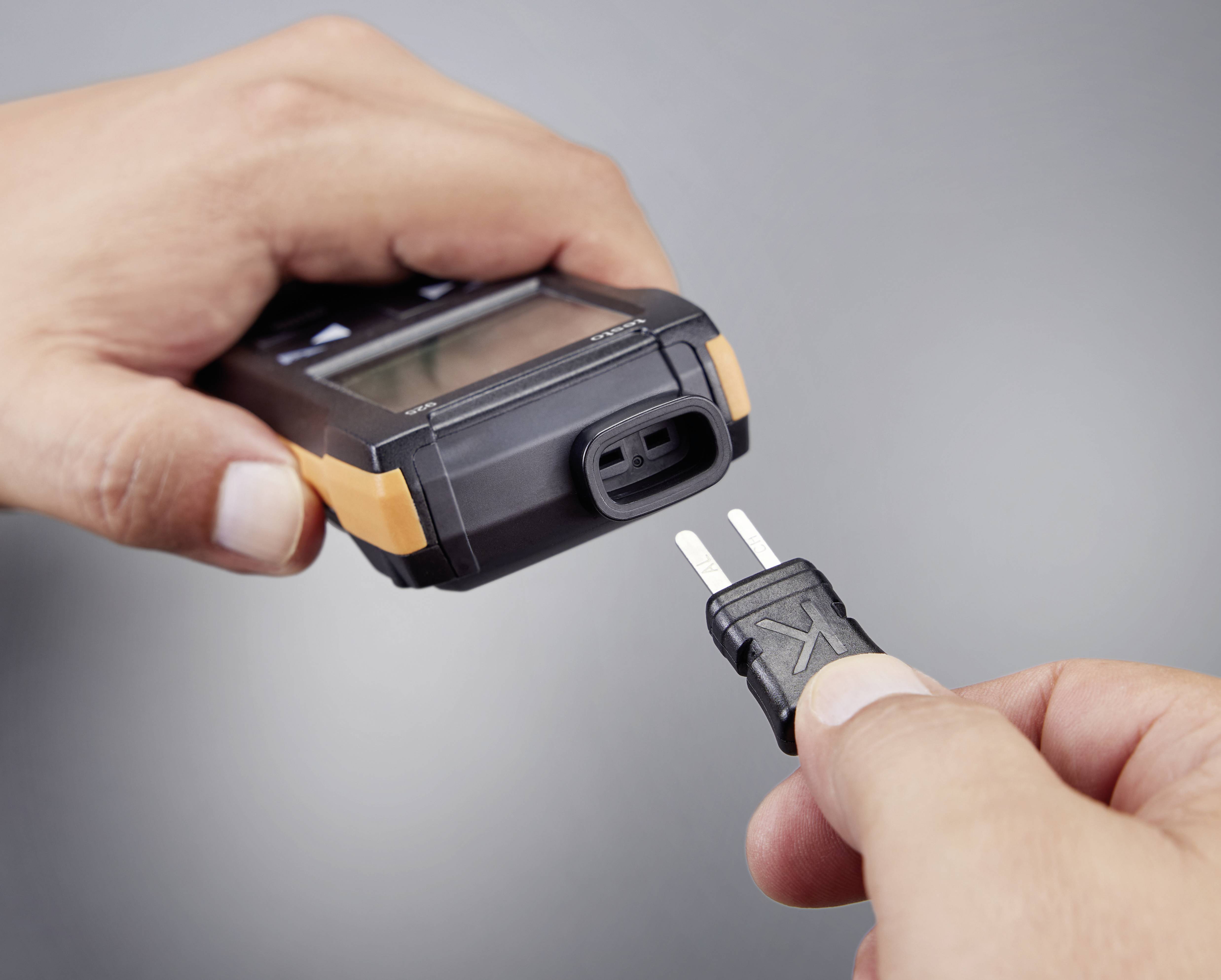 Zwei Hände zeigen ein Thermometer. Eine Hand hält das Gerät, die andere steckt den Sensorstecker in das Thermometer.