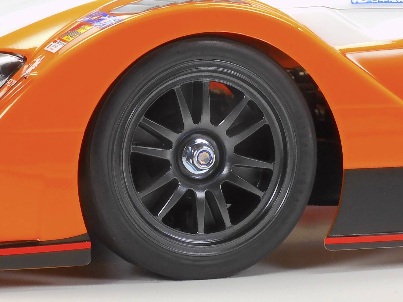 Nahaufnahme eines schwarzen Rennwagenrads mit orangefarbenem Kotflügel, betont Geschwindigkeit und Sportlichkeit.