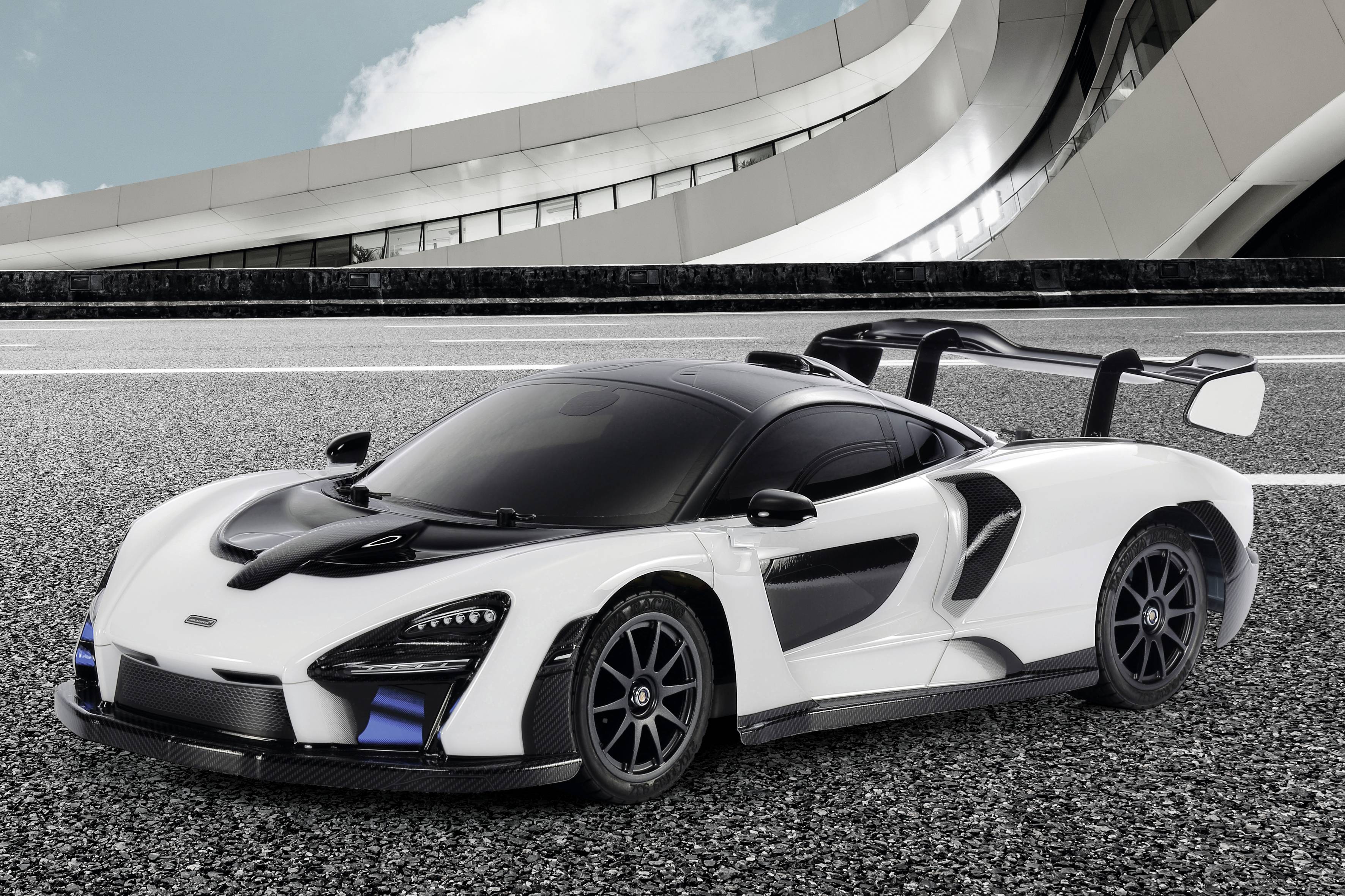 Ein weißer Supersportwagen mit schwarzen Details steht auf einer Straße vor einem modernen, geschwungenen Gebäude.