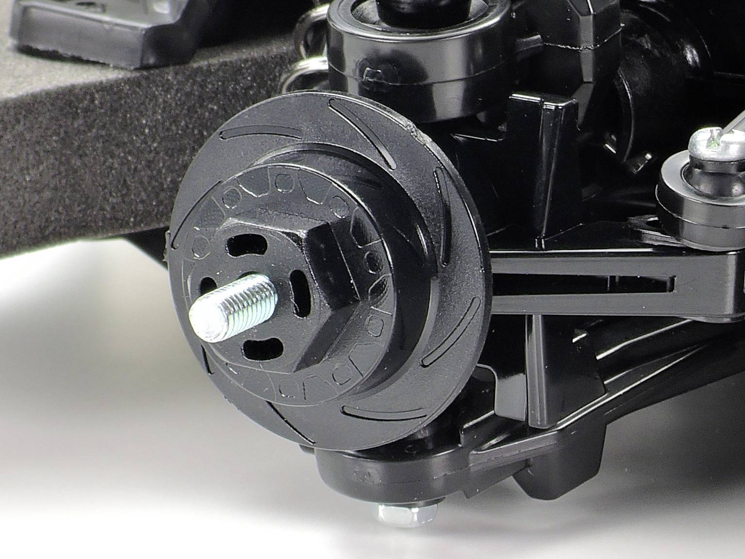 Nahaufnahme eines schwarzen Kunststoff-Rades mit Metallschraube und Aufhängungskomponenten. Mechanische Details hervorgehoben.