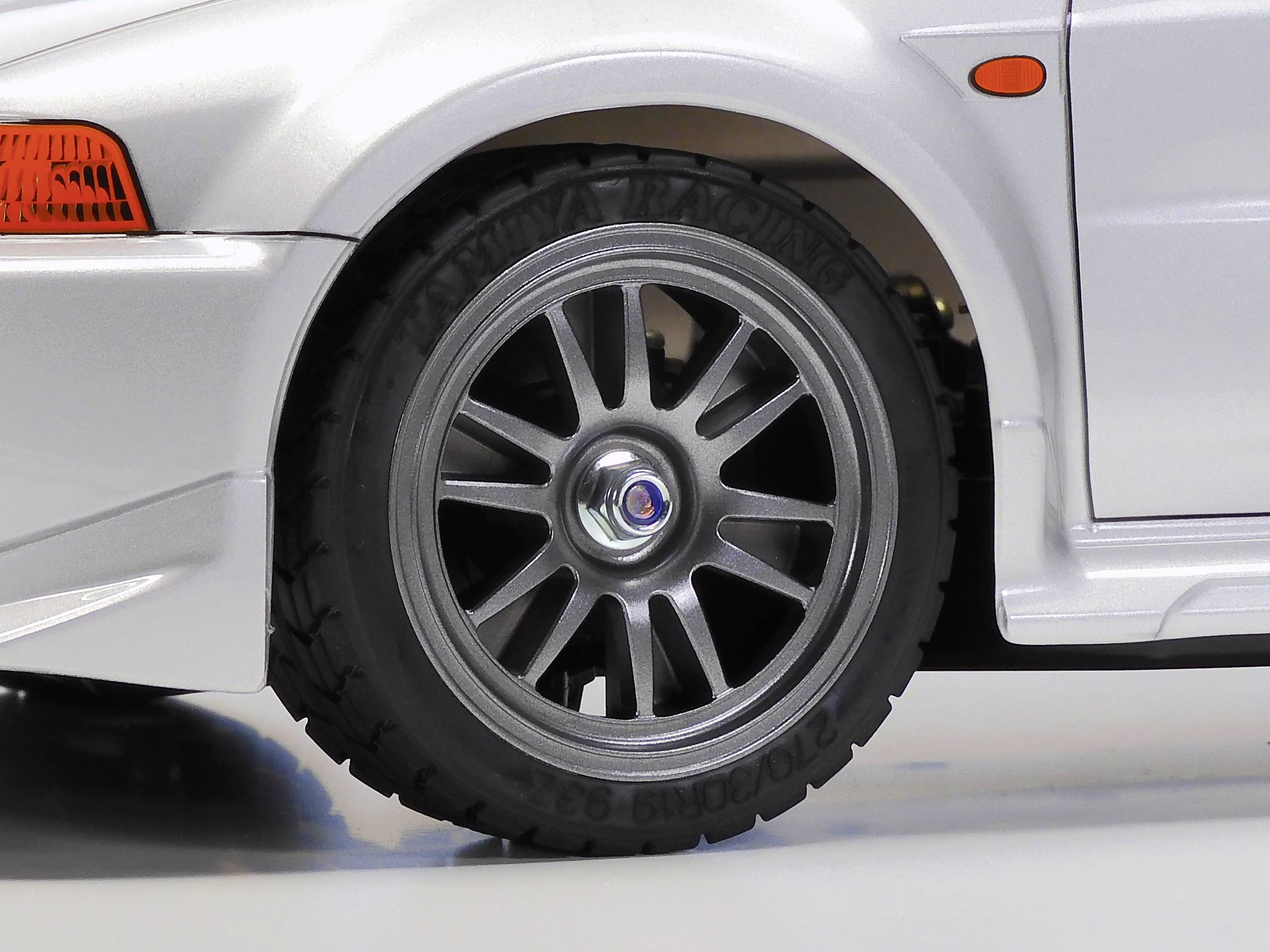 Nahaufnahme eines silbernen Autoreifens mit mehrspeichiger Felge und schwarzer Bereifung auf einem weißen Hintergrund.