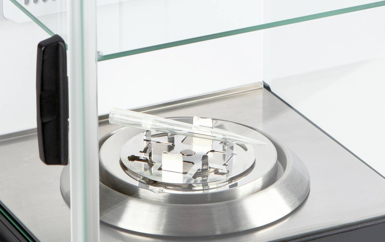 Ein Reagenzglas liegt auf einem Aluminiumträger in einem Glasbehälter, vermutlich in einem Labor.