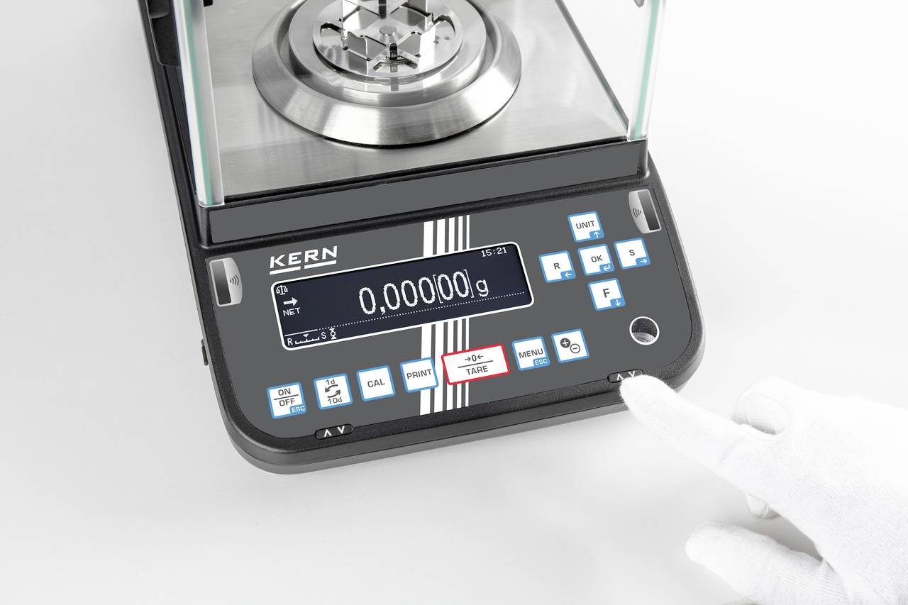Eine elektronische Präzisionswaage mit digitalem Display zeigt '0,00000 g' an. Eine behandschuhte Hand berührt einen Knopf.